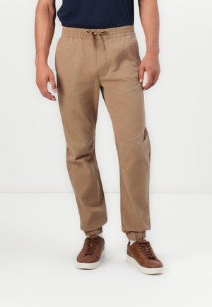 Beige bomulls joggerbukser med elastisk midjebånd og snøring. Mansjetter ved anklene, glatt tekstur og rett passform.