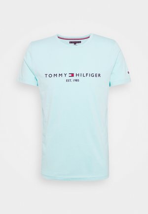 T-shirt in cotone azzurro chiaro con il testo ricamato "TOMMY HILFIGER EST. 1985" in blu scuro e un accento logo rosso e bianco sulla manica.