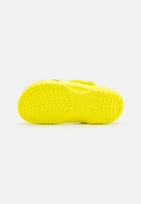 Semelle de chaussure en caoutchouc jaune vif avec un motif texturé et un logo. Présente une forme arrondie et des rainures pour l'adhérence. Pas de matériel visible.