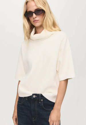 Haut crème à col bénitier avec des manches courtes, texture douce, associé à un jean en denim foncé avec fermeture à bouton et couture contrastante.
