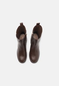 Botas de cuero marrón para tobillo con punta redondeada, cremalleras laterales y textura suave; incluyen un lazo para facilitar el calce.