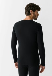Black long-sleeve top made of ribbed fabric, featuring a crew neck and fitted design, shown from the back with long sleeves.