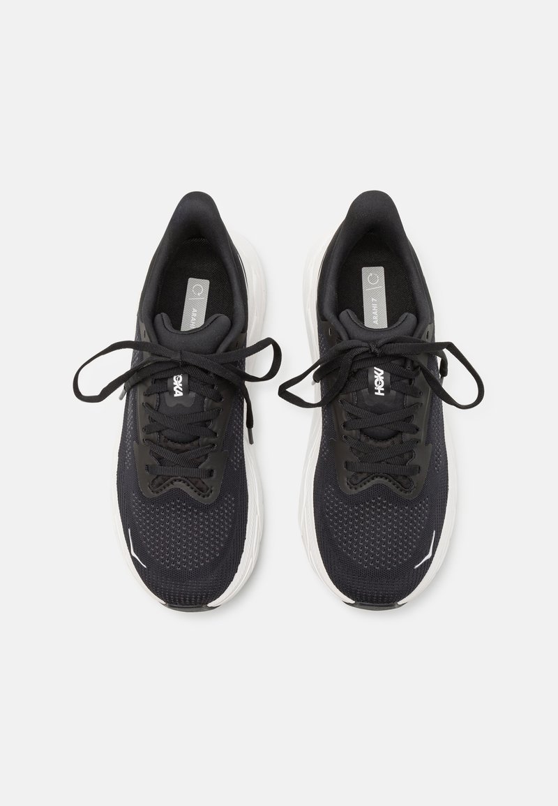 Scarpe sportive nere con tomaia in rete, lacci piatti e accenti bianchi sulla suola e sul lato laterale. Superficie texturizzata per una migliore aderenza.