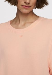T-shirt in jersey color pesca chiaro con collo rotondo, maniche corte e tre linee di cucitura decorative vicino al collo. Texture liscia.