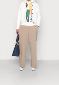 Osoba ubrana w beżowe spodnie szerokie, białe botki za kostkę, białą krótka kurtkę na kolorowy hoodie z grafiką, trzymająca granatową torebkę.