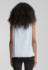 White sleeveless top made of lightweight fabric, featuring a smooth texture, loose fit, and a rounded hemline. No visible hardware or patterns.
