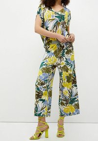 Conjunto con estampado floral que presenta un diseño de pierna ancha en tonos verdes, amarillos y azules; tela texturada; combinado con sandalias de tacón de aguja amarillas brillantes.
