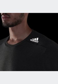 Czarny sportowy t-shirt z okrągłym dekoltem, wykonany z fakturowanej tkaniny, z białymi akcentami logo na lewym ramieniu.
