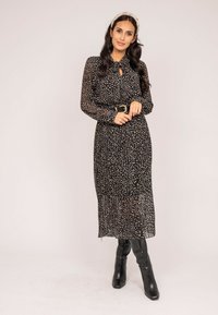 Robe noire à manches longues et à pois, avec une taille cintrée, dotée d'un décolleté en trou de serrure et associée à des bottes noires jusqu'aux genoux.
