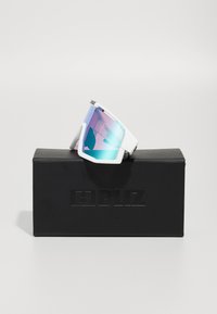 Witte sportzonnebril met een grote, getinte lens die een verloop heeft van blauw naar roze, geplaatst op een zwarte doos met reliëfbranding.