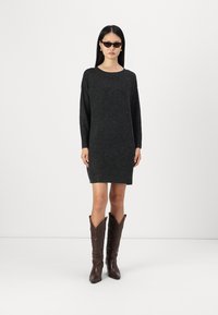 Robe pull tricotée gris foncé avec des manches longues, un col rond et une coupe décontractée. Portée avec des bottes de cow-boy marron ornées de coutures décoratives.