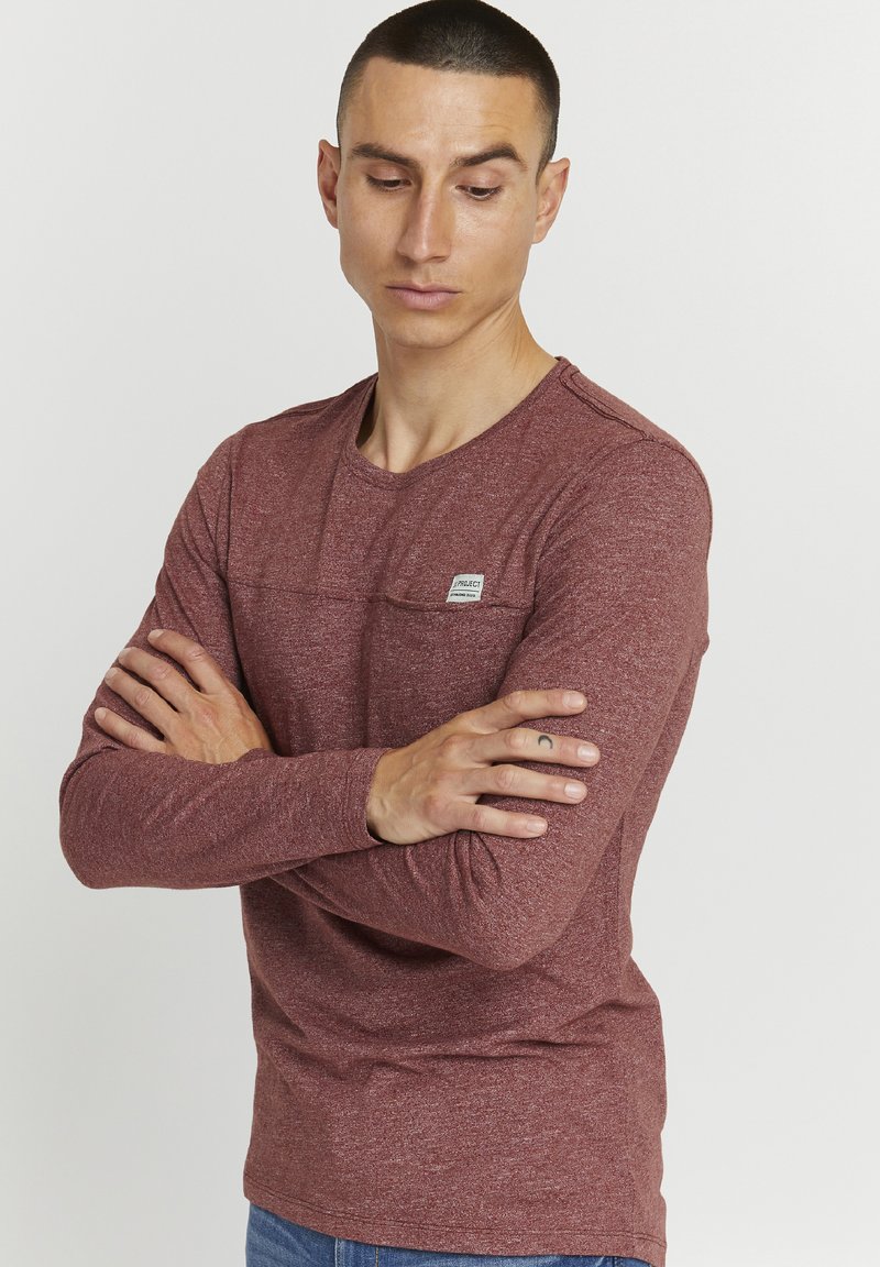 Langermet maroon t-skjorte laget av teksturert stoff, har en lomme på forsiden av brystet, rund halslinning, og en liten merkeetikett på lommen.