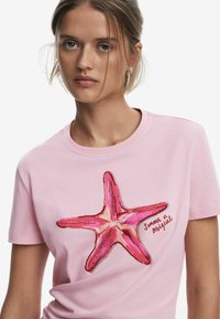 Pink cotton T-shirt featuring a large pink starfish design with red accents and "Summer in Portugal" text. Round neck, short sleeves.