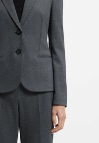 Grijze krijtstreep blazer met twee zwarte knopen, slim fit en notch revers. Glad stof met een subtiele textuur en voorzakken.