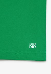 Grünes kurzärmliges Shirt aus atmungsaktivem Material, mit dem Text "ULTRA DRY" in Weiß am Saum, mit einer glatten Textur.