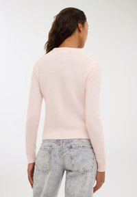 Maglione rosa chiaro con scollatura rotonda, maniche lunghe e polsini a coste. Abbinato a jeans in denim sbiaditi, che mostrano la vista posteriore.