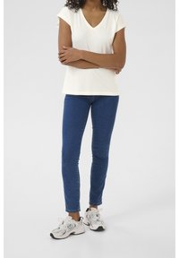 Cremefarvet V-hals T-shirt med korte ærmer, parret med blå slim-fit jeans og hvide sneakers med grå accenter.