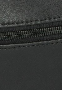 Primer plano de un material sintético negro que muestra una cremallera con una superficie texturizada y costuras en contraste a lo largo del borde.
