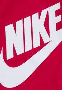Nike márkázás fehér színben egy élénk rózsaszín textil háttéren, merész betűtípussal és kontrasztos swoosh dizájnnal.