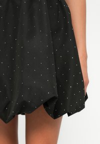 Black skirt featuring a dotted pattern with white and silver accents. The fabric appears smooth with a slightly textured finish.