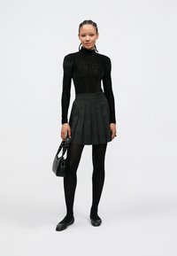 Μαύρο μακρυμάνικο τοπ με σχέδιο λεοπάρδαλης, γκρι πλισέ φούστα, μαύρες καλτσοδέτες και μαύρα φλατ παπούτσια. Περιλαμβάνει μια μικρή μαύρη τσάντα με λουράκι με καρφιά.