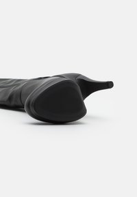 Stivale nero fino al ginocchio con punta appuntita, realizzato in pelle liscia, con suola in gomma testurizzata e un design elegante e aderente.