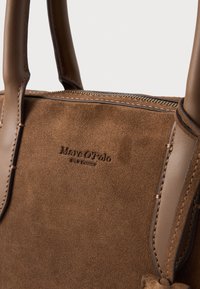 Sac à main en daim marron avec des accents en cuir lisse, des détails cousus et un logo embossé sur le devant. Dispose de poignées arrondies et robustes.