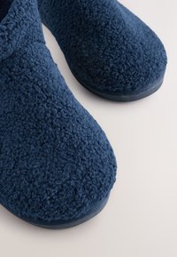 Pantofole blu navy con esterno testurizzato e soffice e punta arrotondata. Tomaia in tessuto morbido con suola liscia e scura.