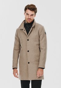 Beżowy płaszcz wełniany z kołnierzem z wycięciem, z guzikami z przodu i dwoma bocznymi kieszeniami. Ma czarną wewnętrzną warstwę i minimalistyczne akcenty.