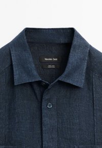 Ciemnoniebieska lniana koszula z ostrym kołnierzykiem, zapięciem na guziki i kieszenią na lewej piersi. Metka informuje "Massimo Dutti, 100% len, wyprodukowano w Chinach."