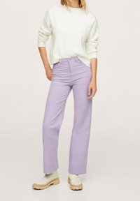 Jean droit lilas à taille haute, associé à un pull blanc. Des bottes beiges épaisses complètent la tenue.