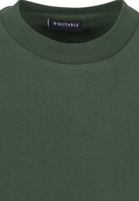 Donkergroen T-shirt met ronde hals gemaakt van katoen. Voorzien van een ribgebreide kraag en het label "SUITABLE" op de halslijn. Zachte, stevige textuur.