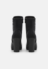 Botines negros de tacón hechos de material sintético con textura suave. Presentan cierre de cremallera y detalles de costuras elevadas en los costados.