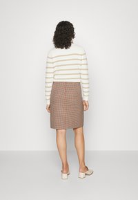 Suéter de rayas crema y marrón, tejido, combinado con una falda lápiz de cuadros marrón, con un corte recto y longitud hasta la rodilla. Zapatos sin cordones en marfil.