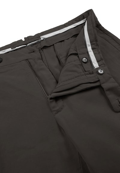 Primer plano de pantalones gris oscuro que muestran una cremallera abierta, una tapeta con dos botones y una cinturilla elástica con un forro interior a rayas.