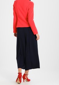 Top de manga larga rojo combinado con pantalones de pierna ancha azul marino y zapatos de tacón rojos. La tela del top tiene un acabado texturizado.