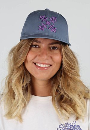 Casquette gris charbon avec broderie florale violette sur le devant ; visière courbée ; portée sur une chemise blanche avec un design graphique.
