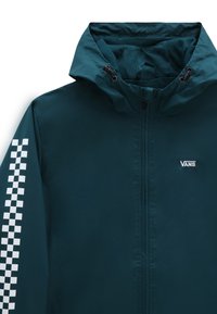 Chaqueta impermeable de color verde azulado con capucha. Presenta un patrón de cuadros blancos en la manga izquierda y un logo en el pecho. Interior texturizado.