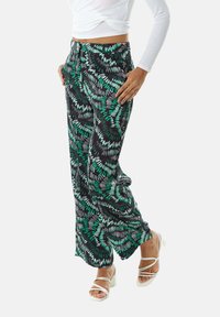 Black pants with a green leaf pattern, made of lightweight fabric. Features a straight cut and side pockets. Worn with white strappy heels.