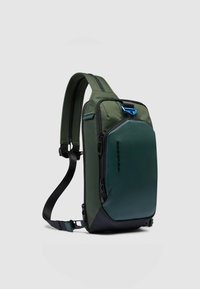 Mochila verde con una mezcla de tejido texturizado y secciones lisas, que cuenta con un tirador de cremallera azul y una correa de hombro ajustable.