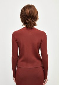 Prążkowany bordowy sweter z długimi rękawami i zaokrąglonym dekoltem, z teksturowanymi detalami na ramionach i plecach.
