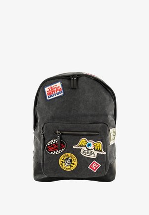 Sac à dos en tissu noir avec divers patchs brodés. Il possède une poche zippée à l'avant et un dessus arrondi, avec des bretelles solides.