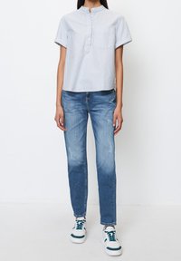 Kortärmad, kragad skjorta i ljusblå och vit randig design, ihop parat med slitna blå jeans och vita sneakers med gröna detaljer.