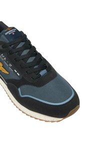 Scarpa da ginnastica con tomaia in mesh blu navy, dettagli in suede nero, lacci scuri e suola bianca testurizzata con battistrada marrone. Dettaglio del logo in ottone visibile.