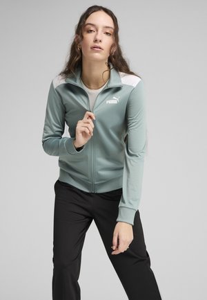 Chaqueta de cremallera en un tono azul verdoso claro con detalles en blanco, hecha de una tela suave. Presenta un cuello alzado y un logo en el pecho.
