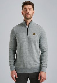 Lichtgrijze rits-trui met een gestructureerd patroon, ribgebreide manchetten en zoom, en een klein zwart logo-oppatch op de borst.