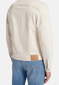 Giacca di Jeans chiara con design classico, caratterizzata da un'etichetta in pelle in vita e dettagli cuciti sulle tasche posteriori.