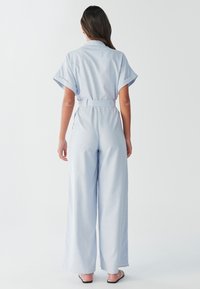 Mono azul claro con cinturón, mangas cortas, pantalones de pierna ancha y cuello con solapa. Presenta un diseño de ajuste holgado y textura suave.