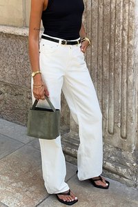 Witte high-waisted jeans, aansluitend zwart tanktop, zwarte riem, groene suède handtas, zwarte flip-flops met witte pedicure, gouden sieraden accenten.