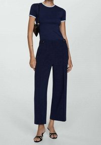 Haut marine à manches courtes avec des bordures bleu clair, associé à un pantalon large taille haute en marine avec des boutons sur le devant et un tissu lisse.